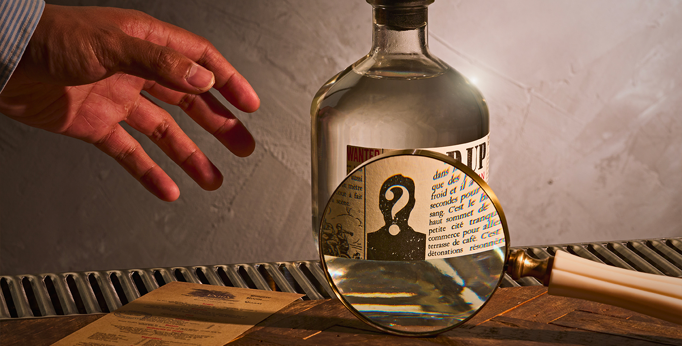 Photo du gin Hold Up, une loupe zoom sur l'étiquette, une main s’apprête à prendre la bouteille de gin
