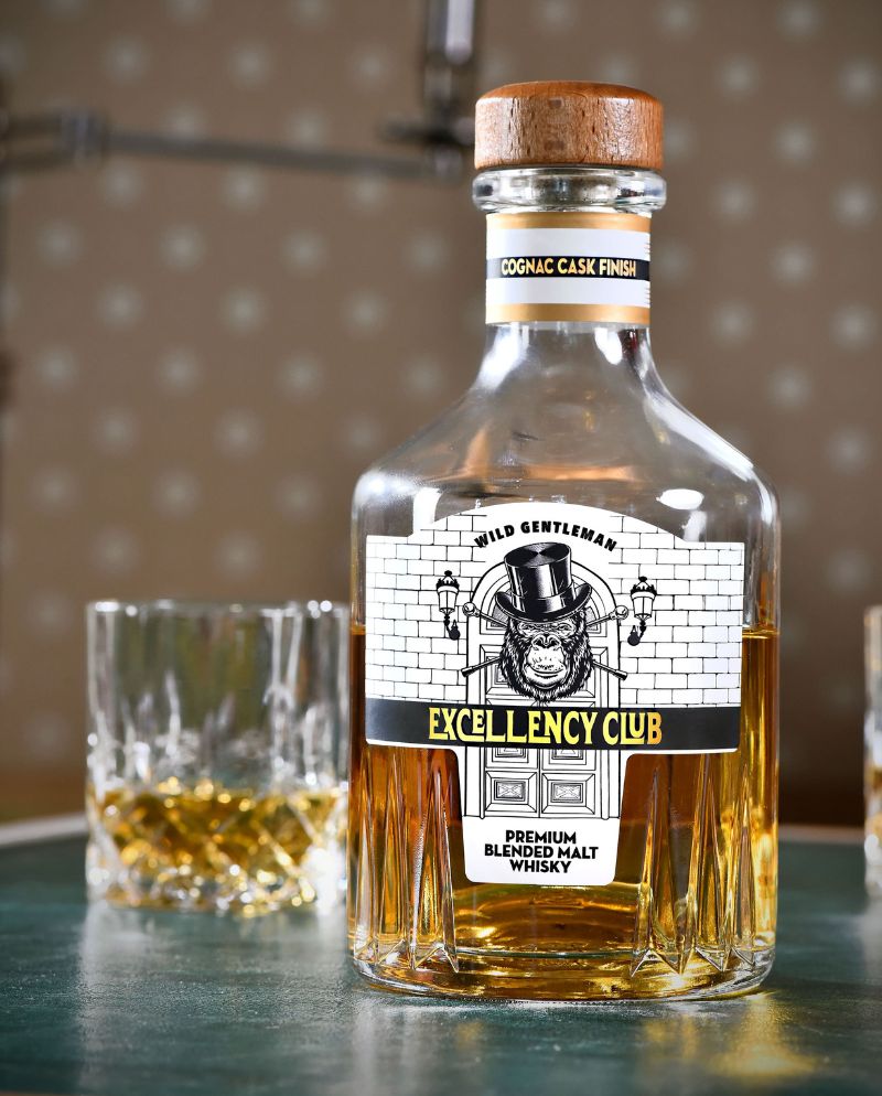 Photo du whisky blended malt Excellency club cognac cask finish avec un verre de whisky en fond